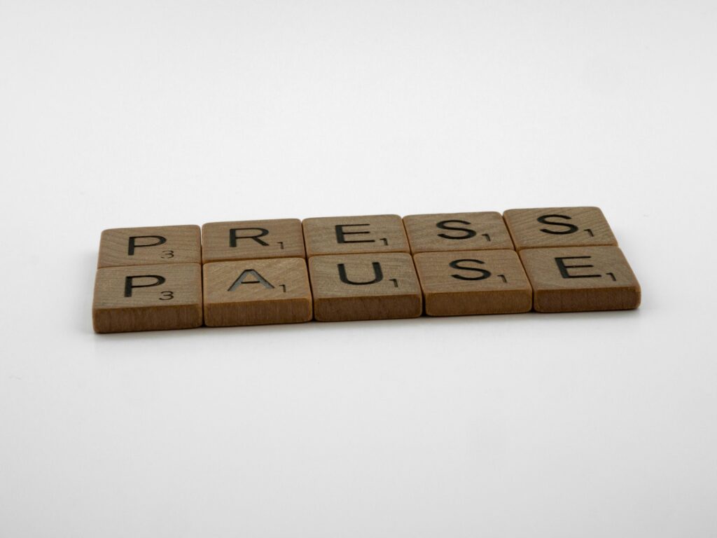 Wooden Scrabble tiles arranged to spell 'Press Pause' on a clean white background.