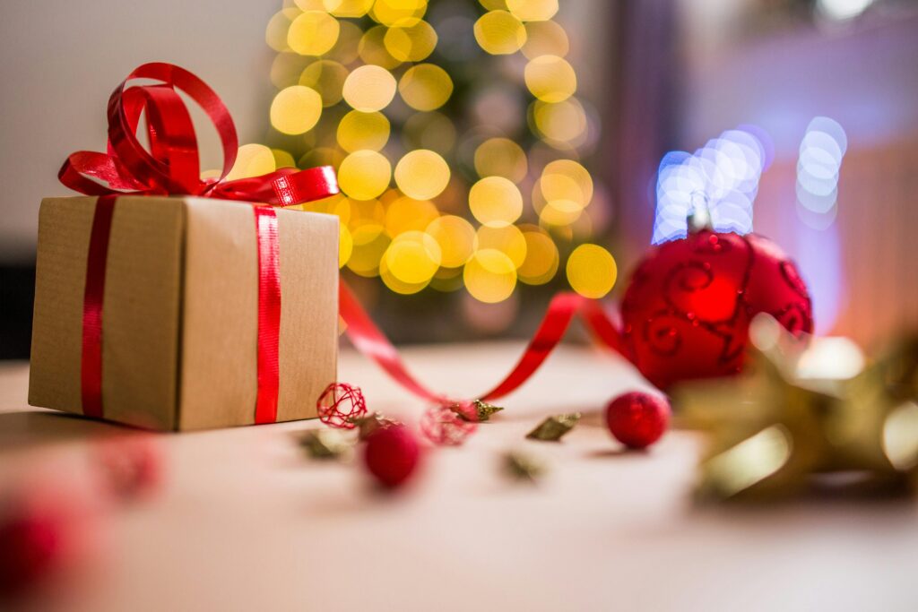 A beautifully wrapped Christmas gift with festive decorations and bokeh lights in the background, creating a warm holiday atmosphere.